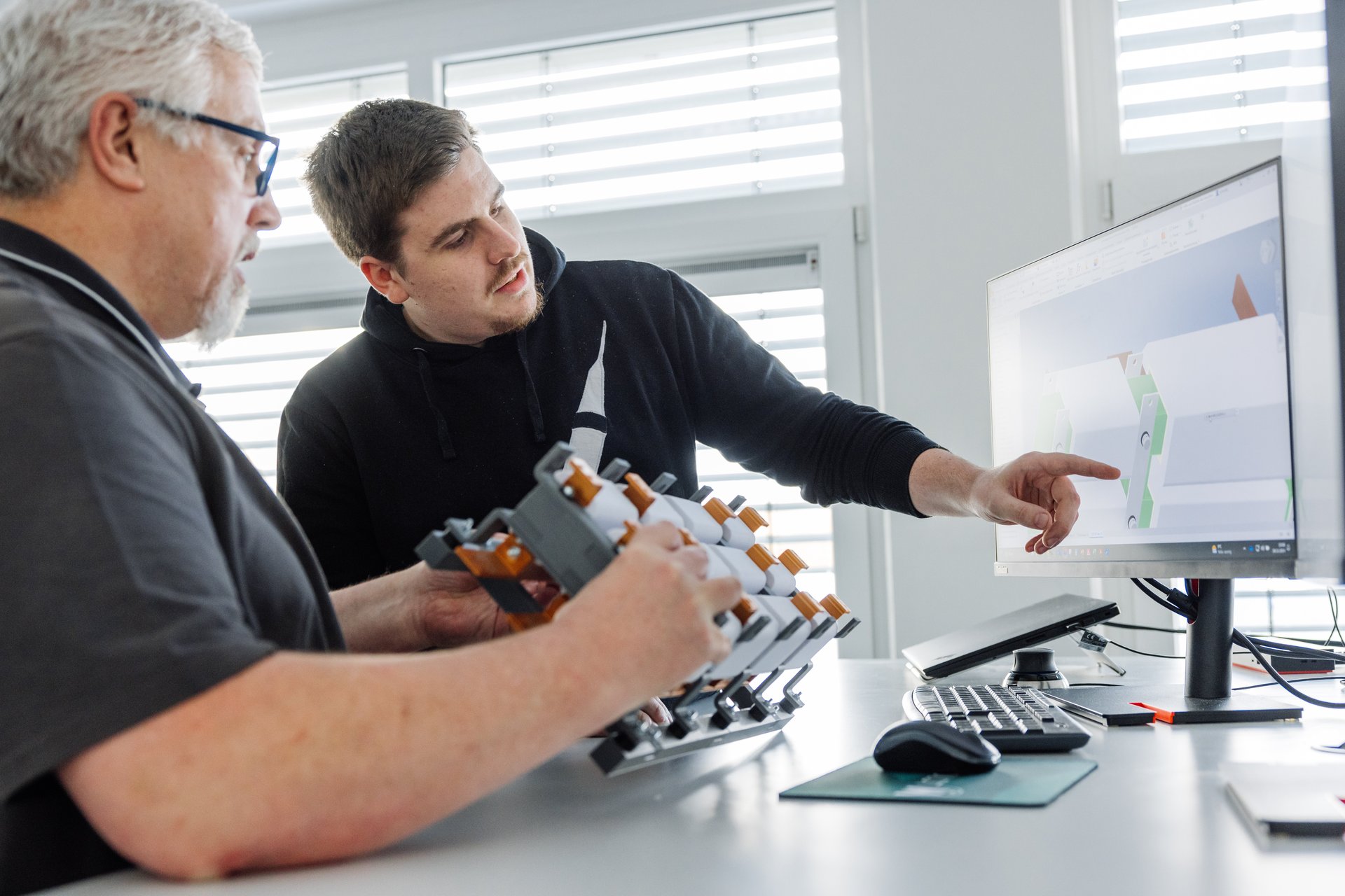 Zwei Mitarbeiter bei der Entwicklung – Diskussion eines Transformatormodells am Computer mit physischem Prototyp in der Hand.