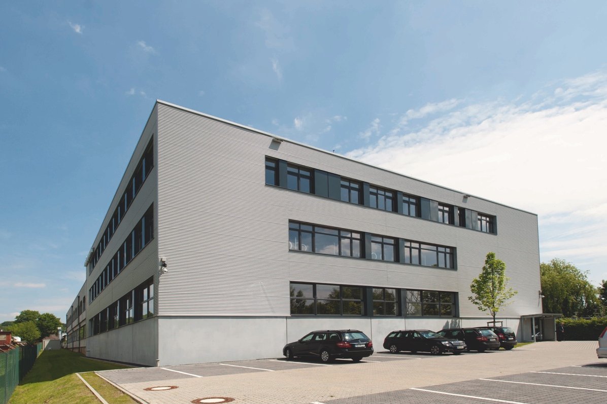 Mangoldt's modern headquarters in Aachen – a three-story building with large windows and adjacent parking lot